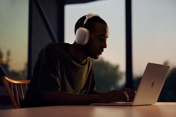 A man wearing Apple AirPods Max headphones while using a MacBook