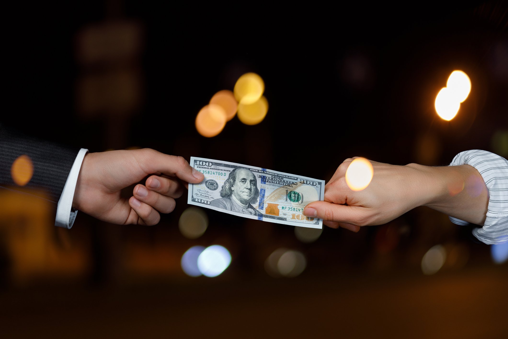 Two hands playing tug of war with a $100 bill. 