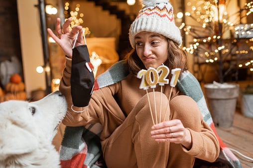 A person ringing in 2021 with a dog and a facemask she's holding in disdain.