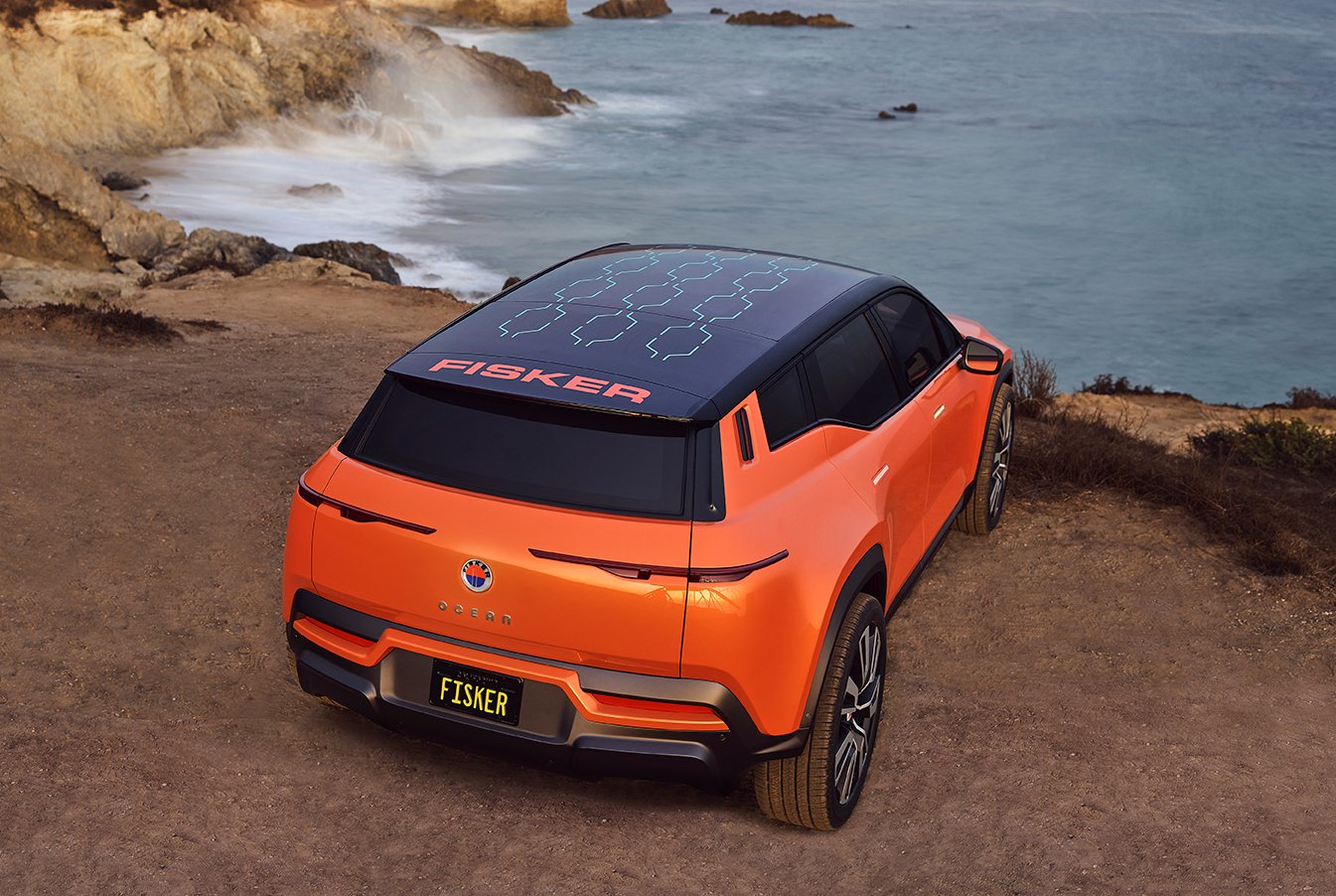 An orange Fisker Ocean, an electric SUV, parked on a waterfront.