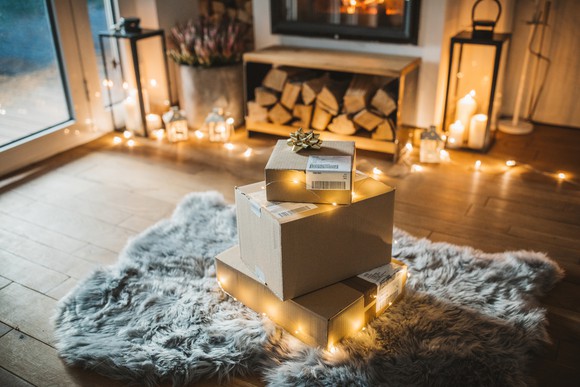 Pile of mail packages on rug surrounded by string lights. Fireplace and lit candles in the background.