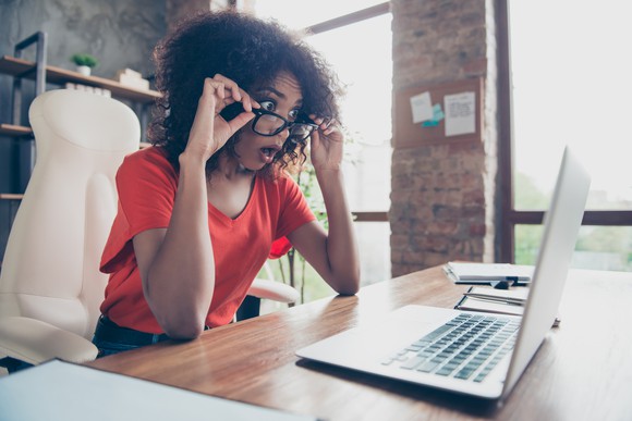 A panicked woman looks through her glasses at her laptop.