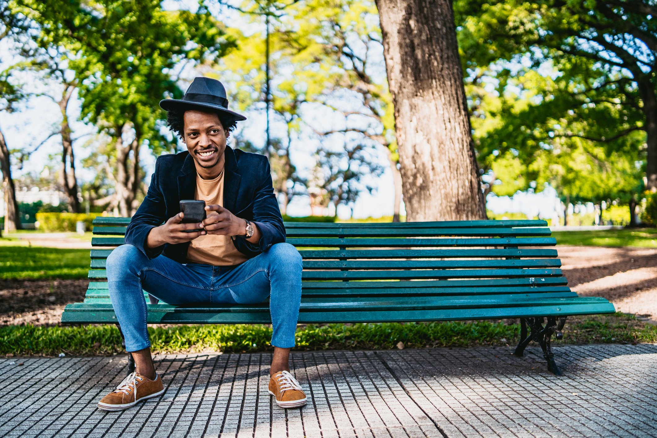 A smiling man sits on a park bench with his phone.