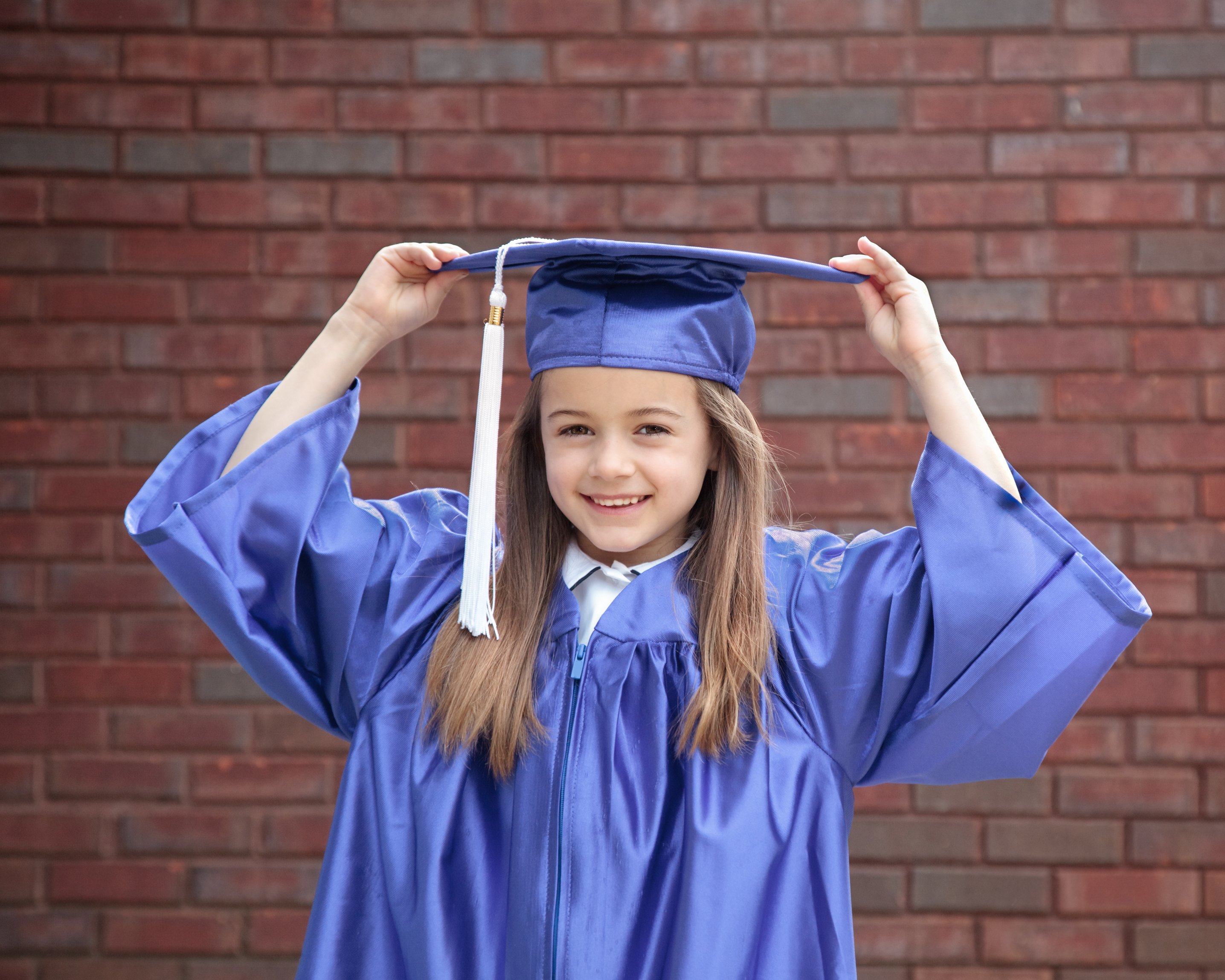 A happy child graduate smiles in her cap and gown.