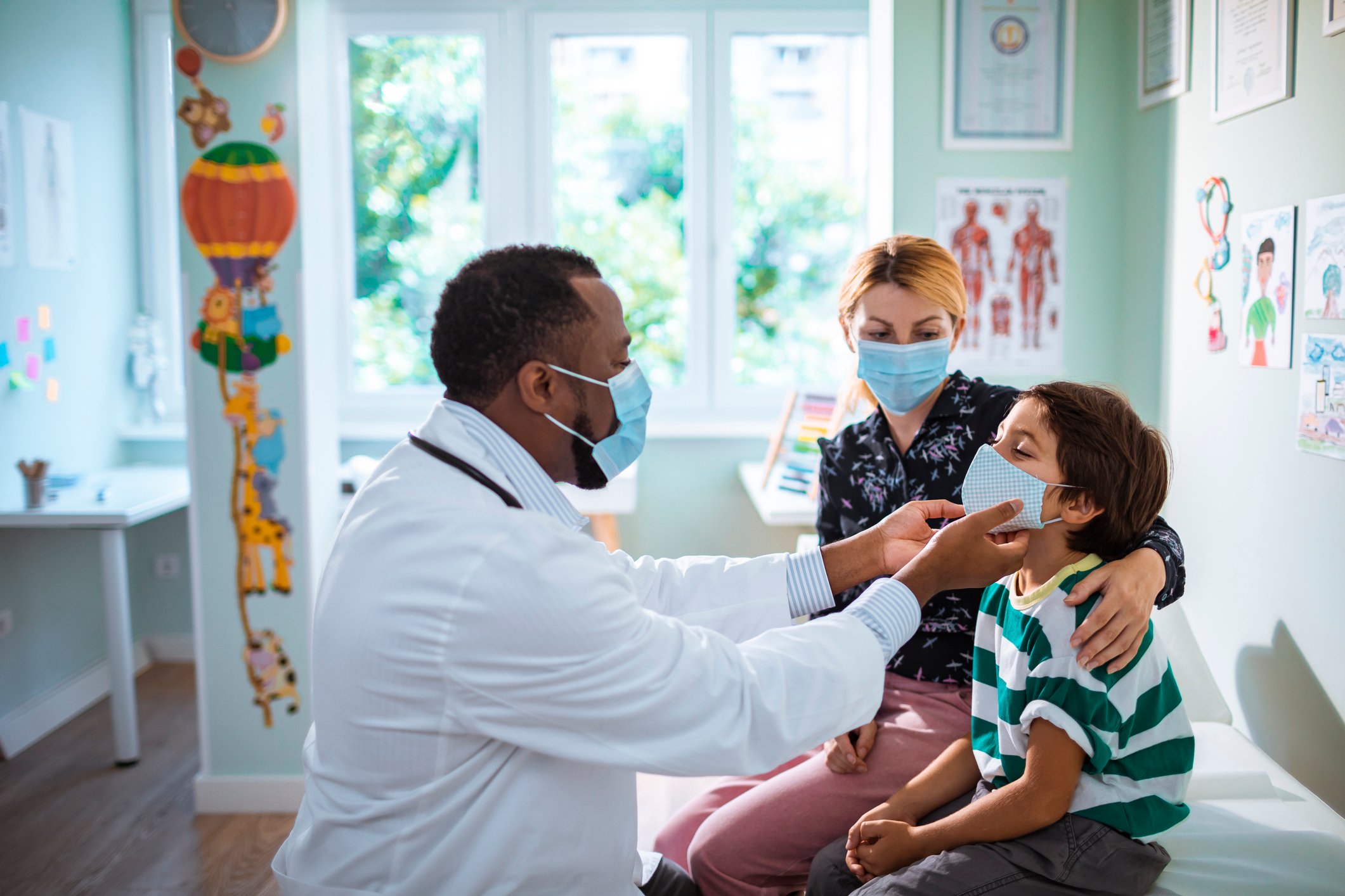 pediatrician in a doctor's office examines a little boy as he sits next to his mother 