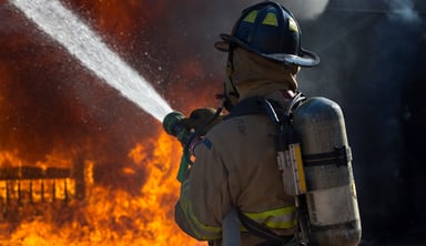 A fireman pointing a spraying hose towards a fire