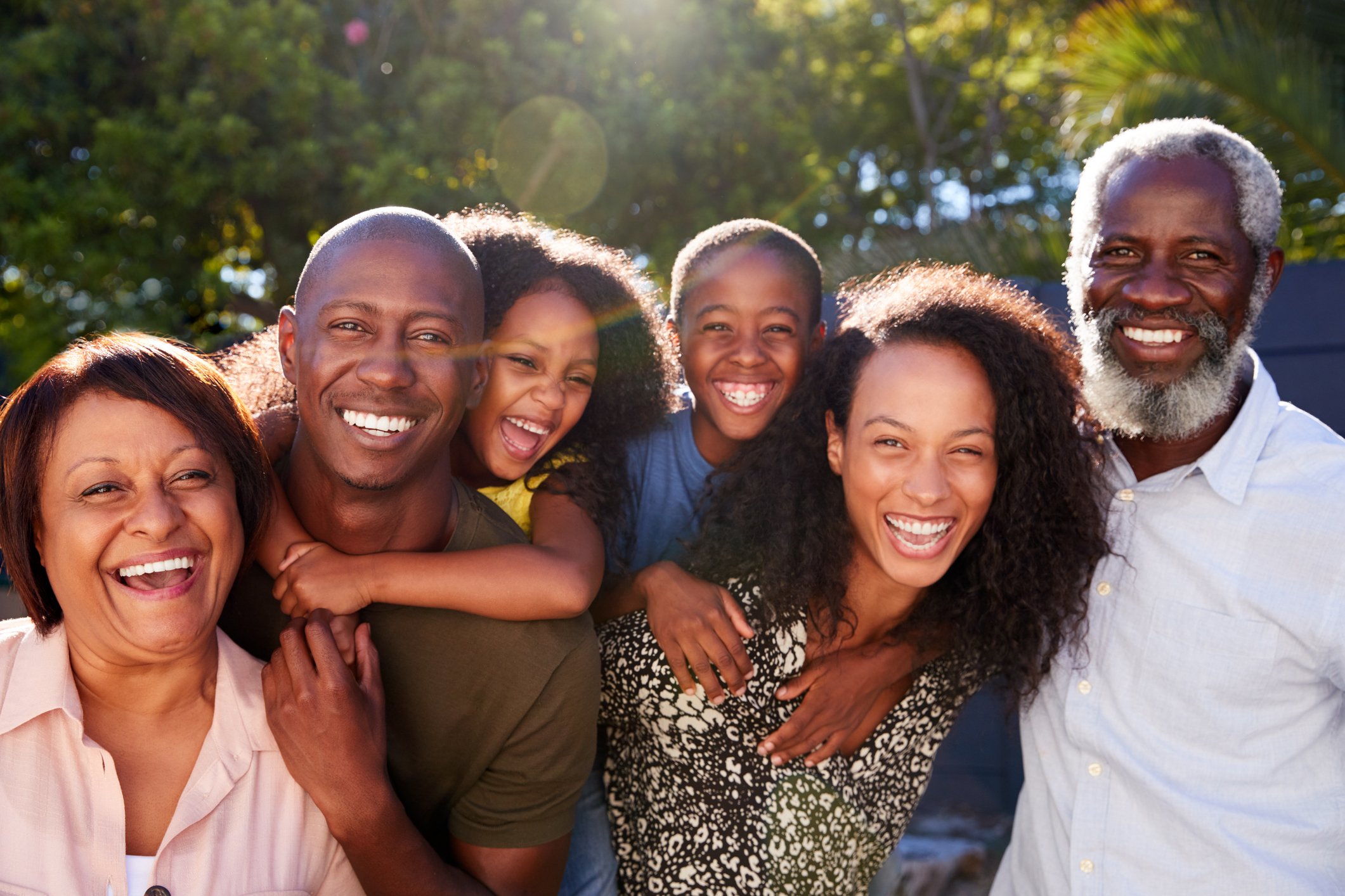 Multi-generational family in garden at home against flaring sun.