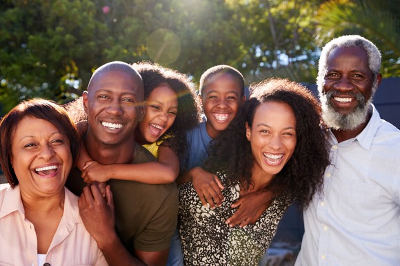 Multi-generational family in garden at home against flaring sun.