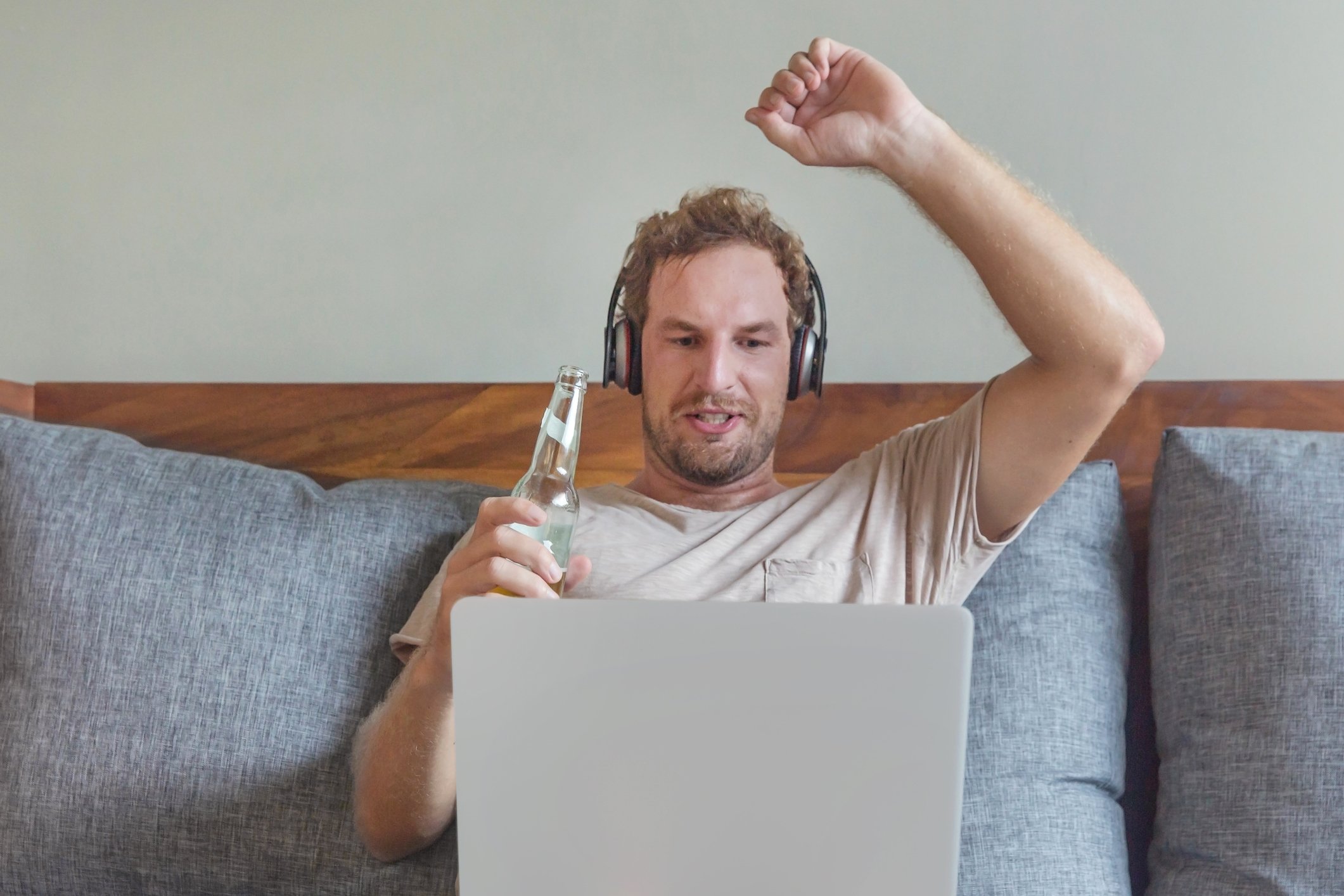 man with headphones on couch streaming sports and drinking a beer