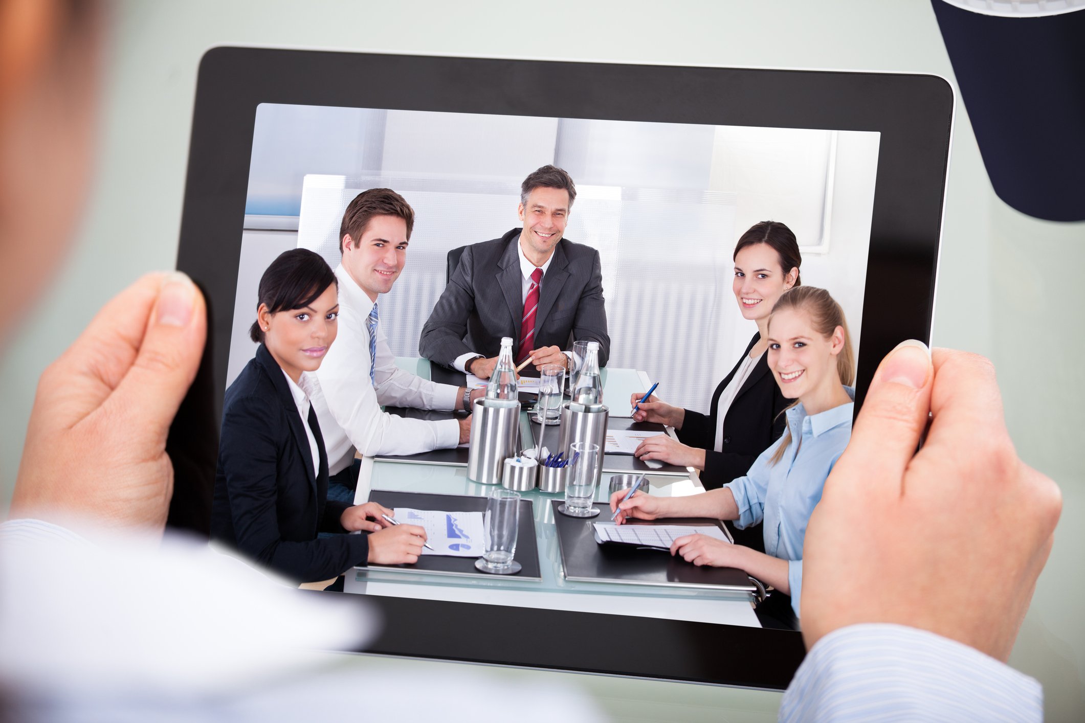 Two hands holding a tablet computer showing a video conference.