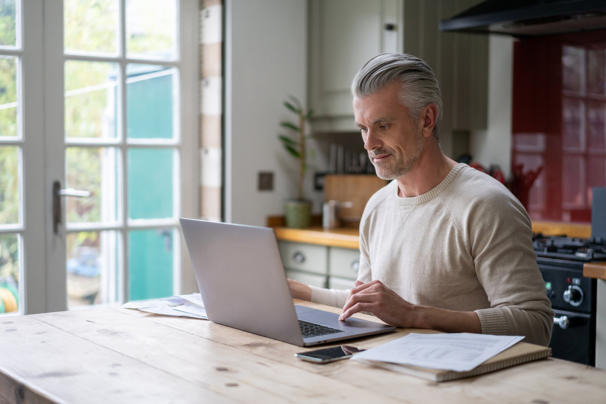 A middle aged man smiles at his laptop at home. 