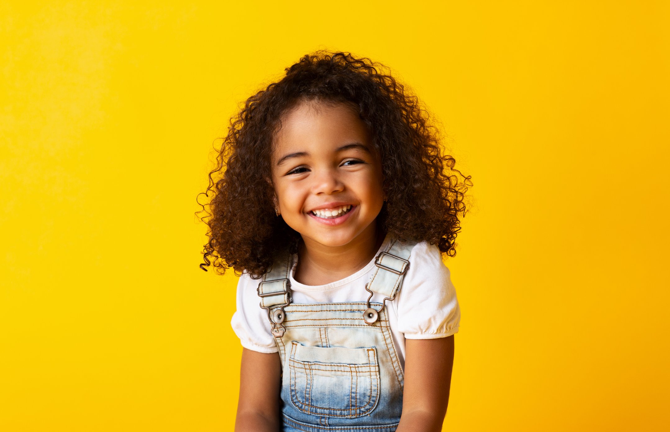 Little girl smiling in front of yellow background. 