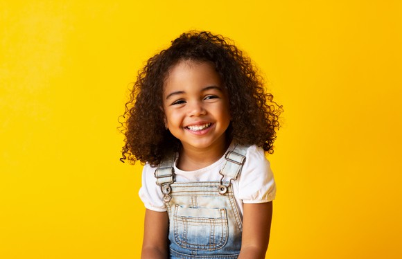Little girl smiling in front of yellow background. 