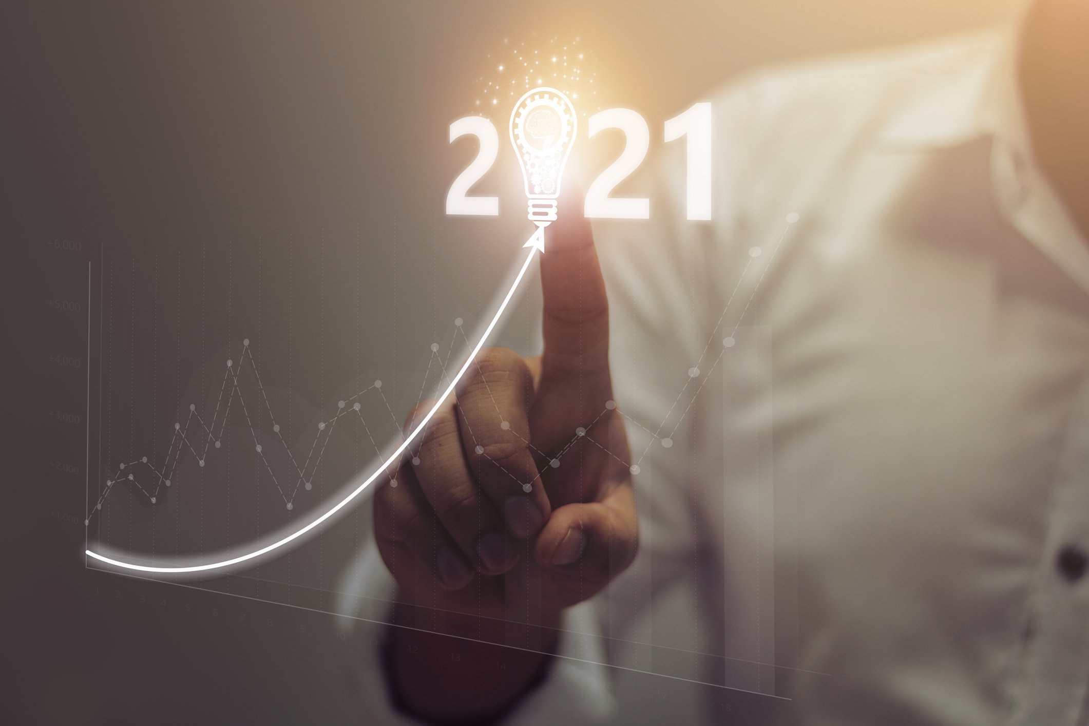 A person pointing to an image of 2021 with a light bulb in the place of the zero next to a line trending upward 