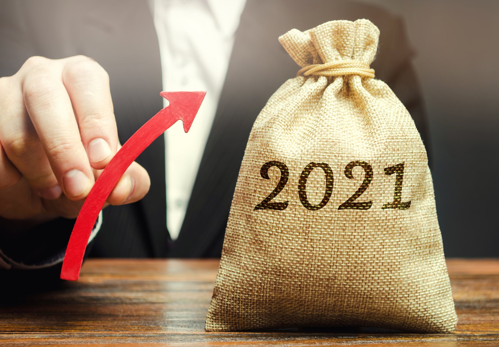 Person holds upward arrow next to moneybag with 2021 printed on it