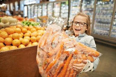 A young girl holding a bulk package of carrots