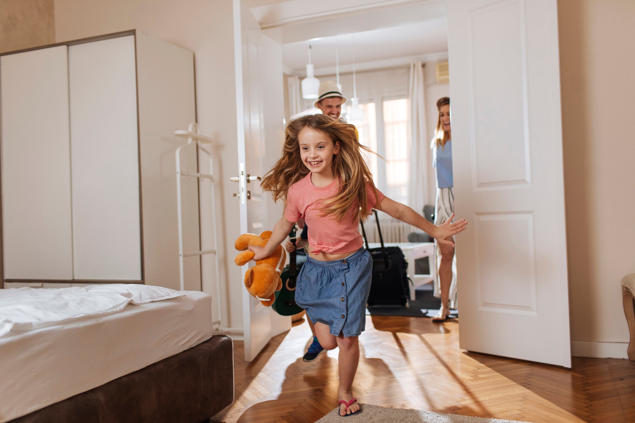 Young girl running anxiously into her room at a vacation home as her parents watch in the background.