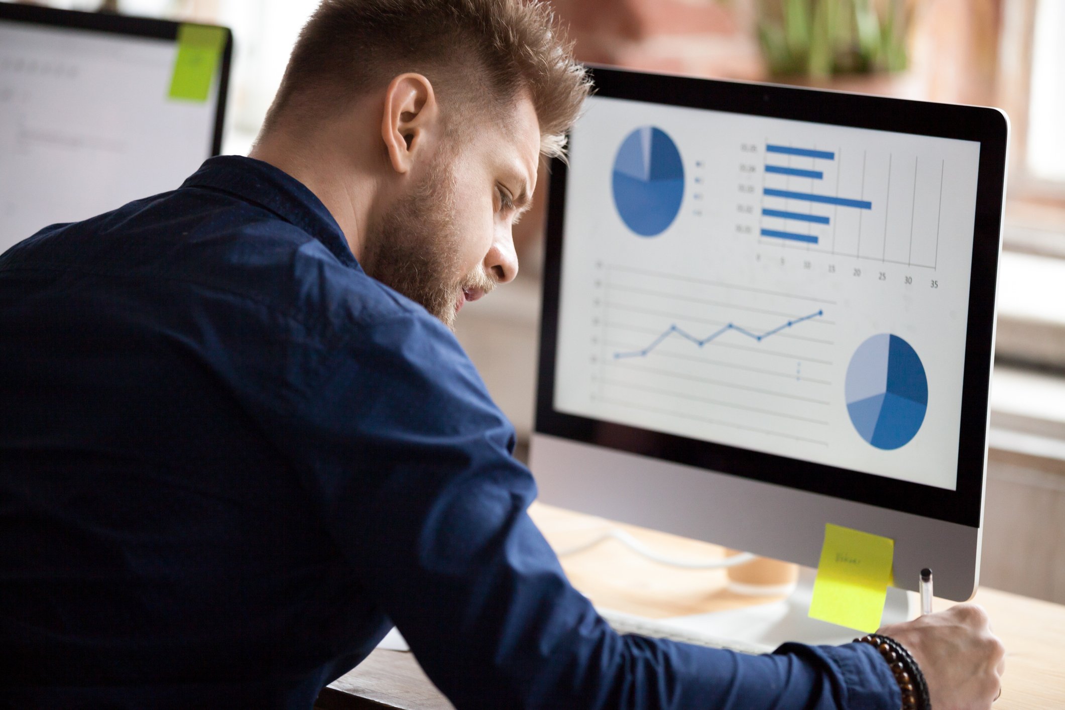 Man at desk looking over investments on computer screen.