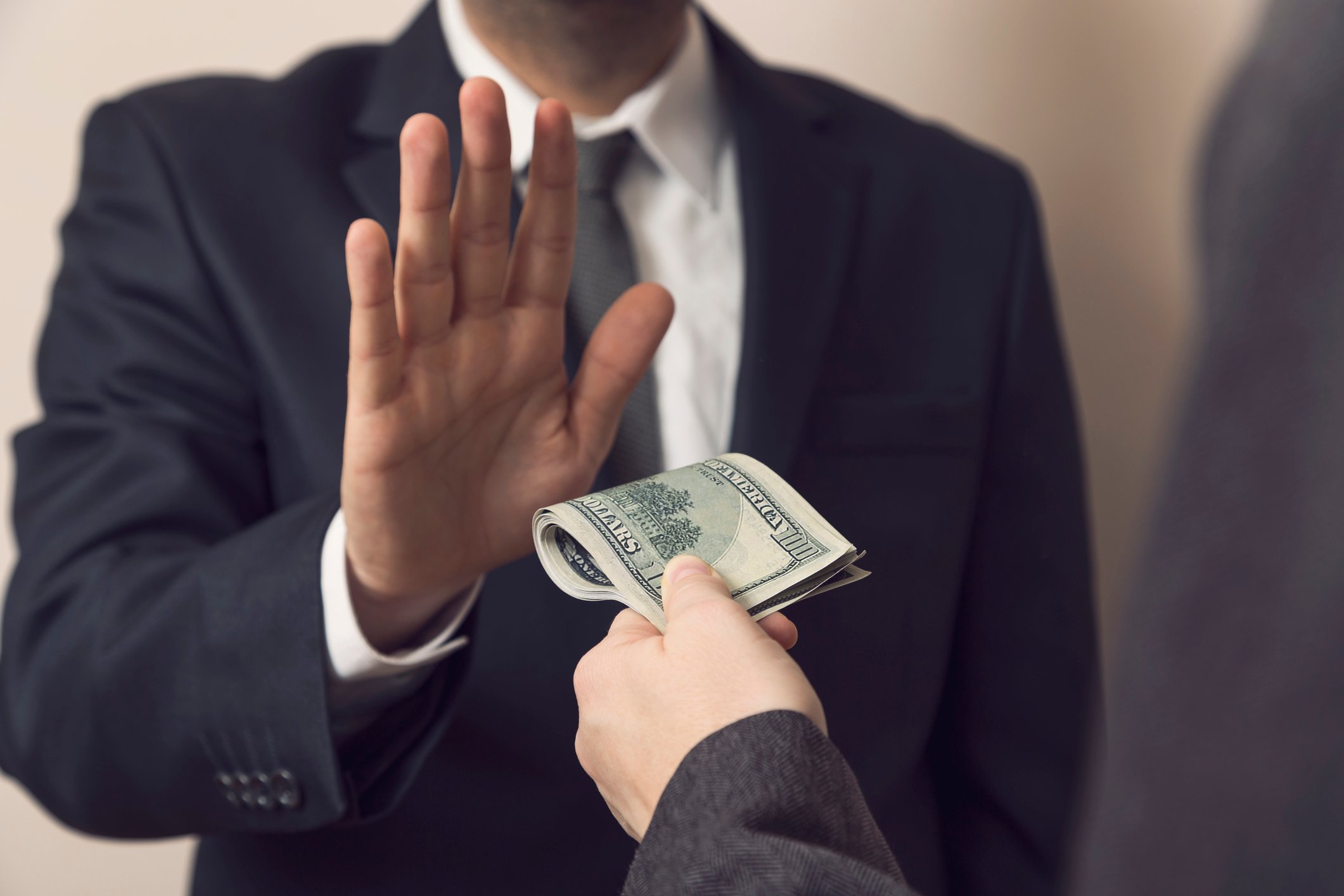 Man in suit holding hand up against another hand offering cash