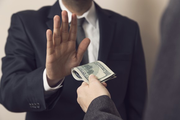 Man in suit holding hand up against another hand offering cash