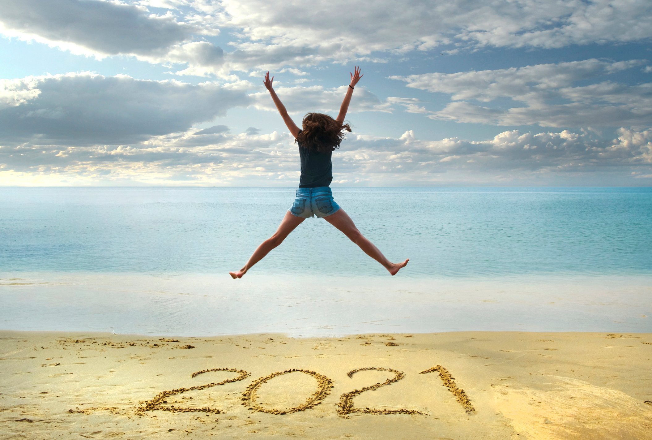 A woman jumping up in the air with 2021 written on the beach sand.
