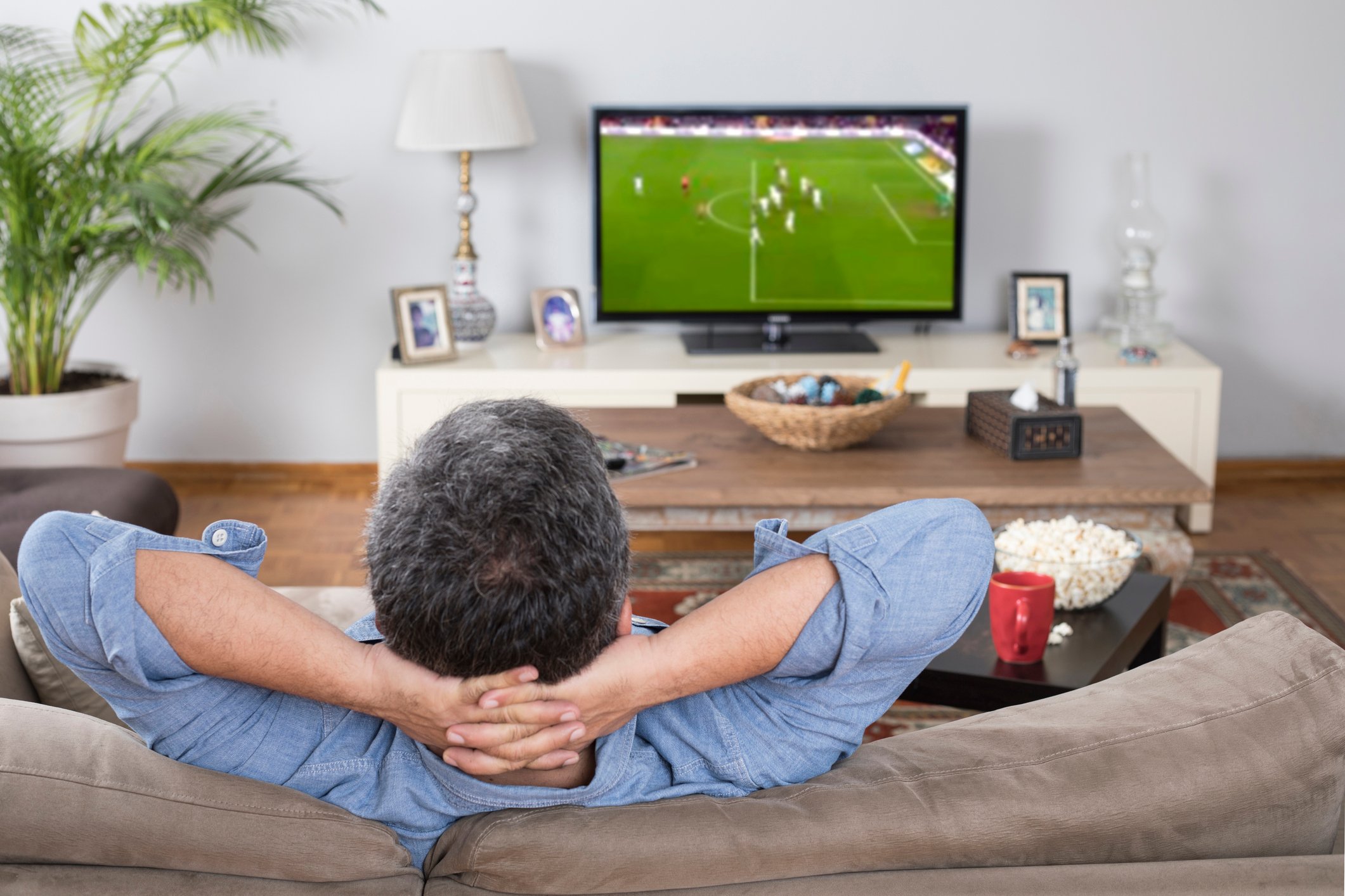 Man in a sofa watching a soccer match on TV.