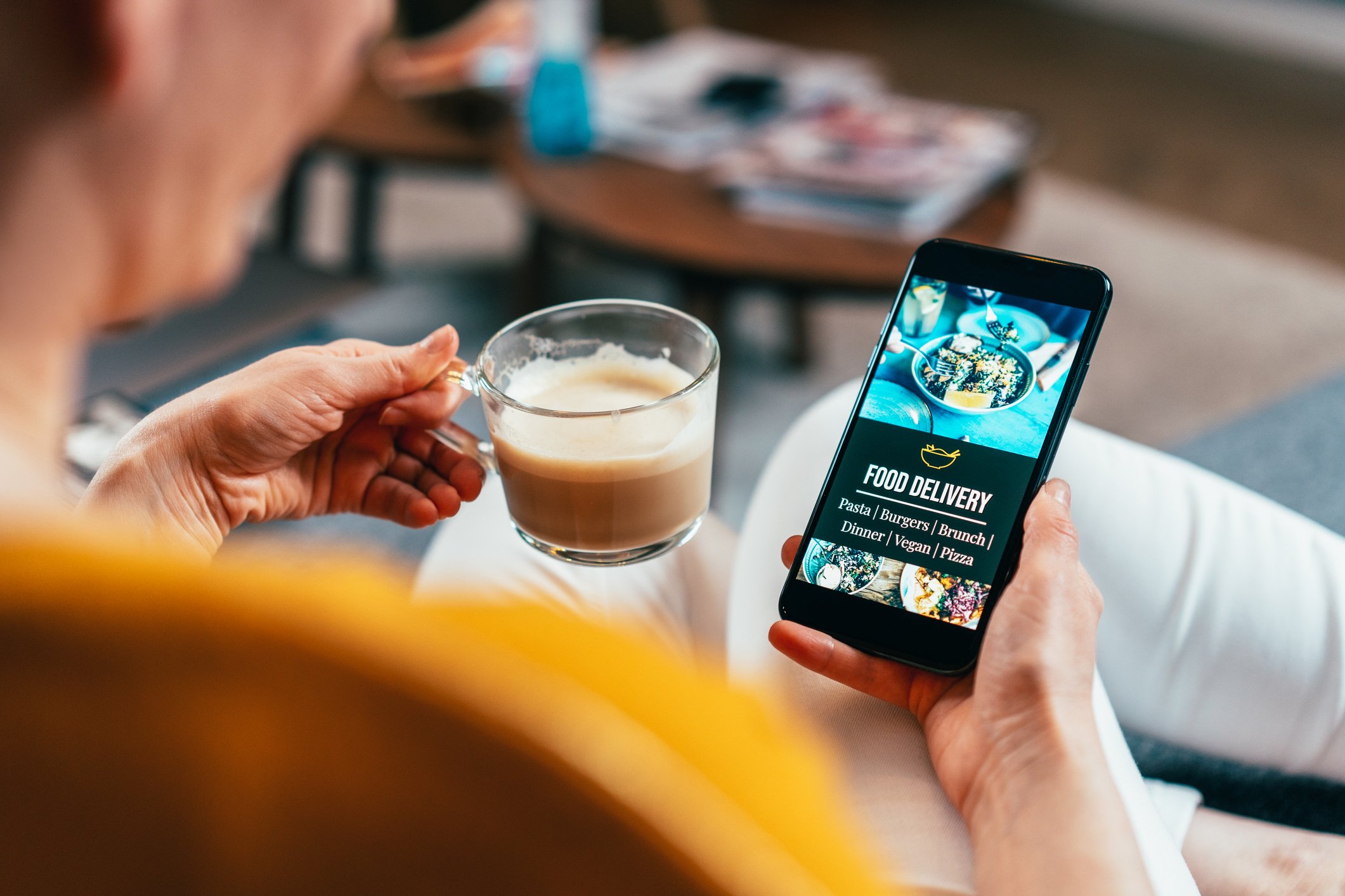 A person orders food on a phone while drinking coffee.