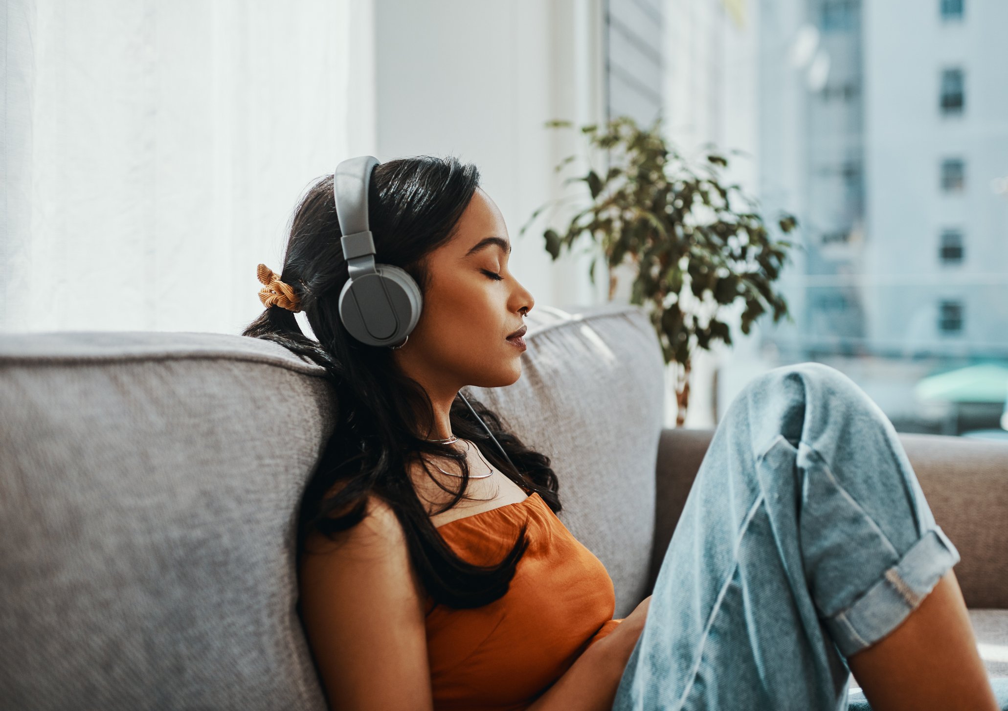 A woman sitting on a couch with headphones on and her eyes closed