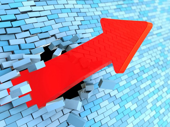 A red charting arrow smashes upward through a blue brick wall.