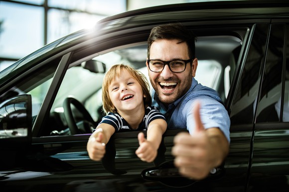 Parent and child in the driver's seat of a car, smiling and giving the thumbs-up.