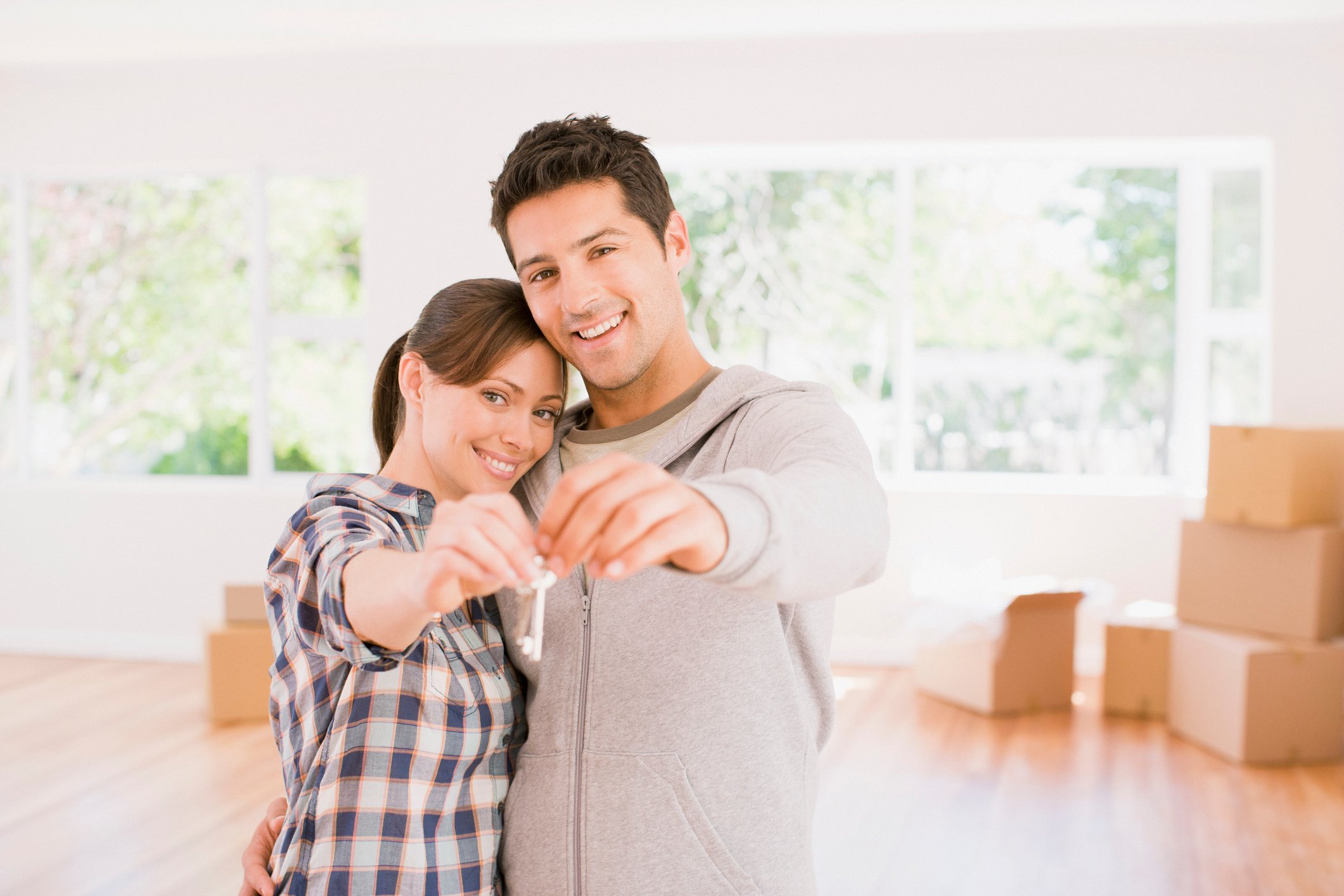 A couple holding up a key inside a home, with packed boxes in the background. 