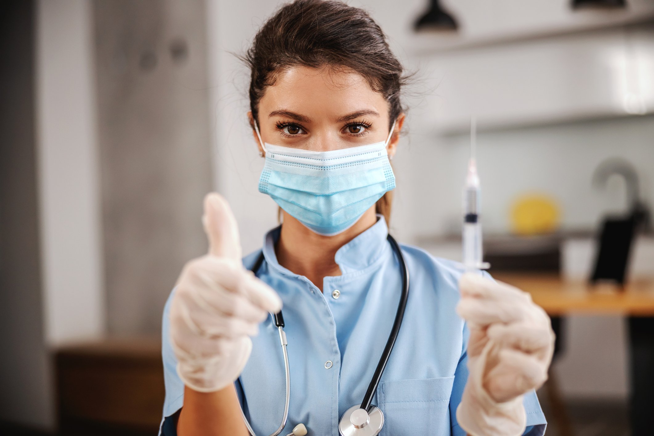 Healthcare worker wearing a mask giving a thumbs up while holding a syringe. 