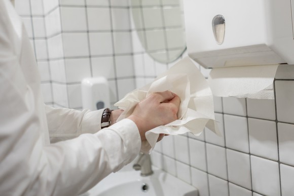 Person drying hands with tissue paper while standing beside a tissue dispenser