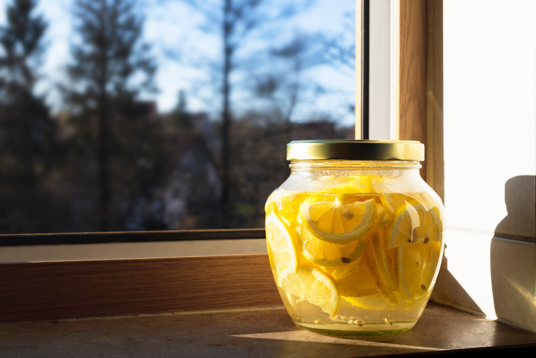 A jar of lemonade next to a window.