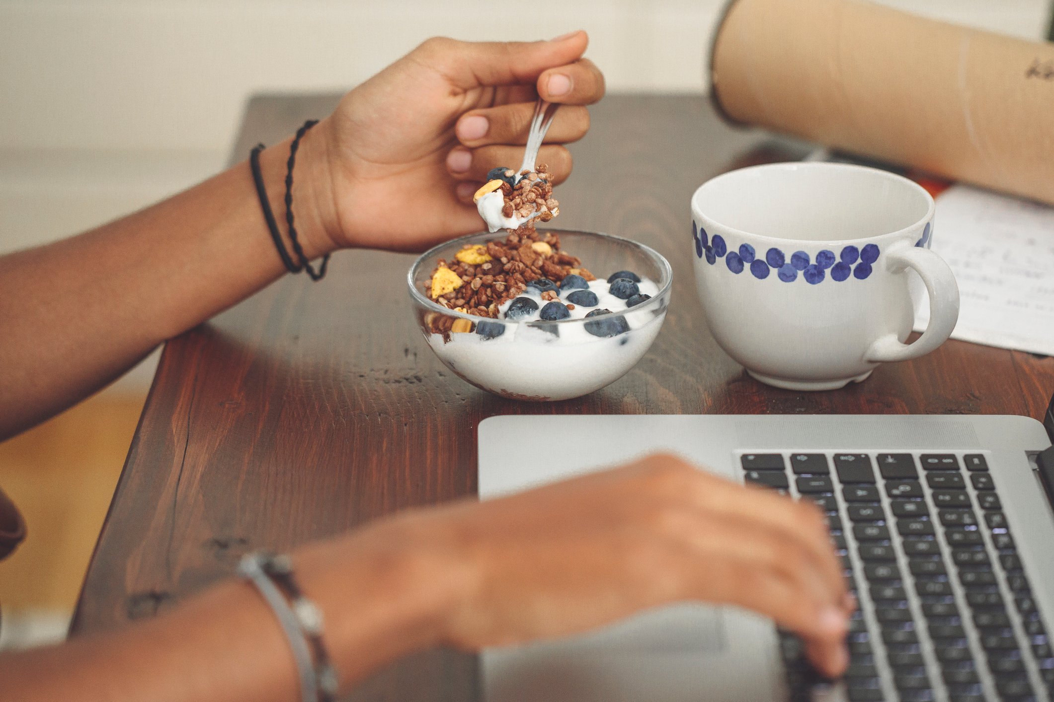 Someone eating cereal and using laptop