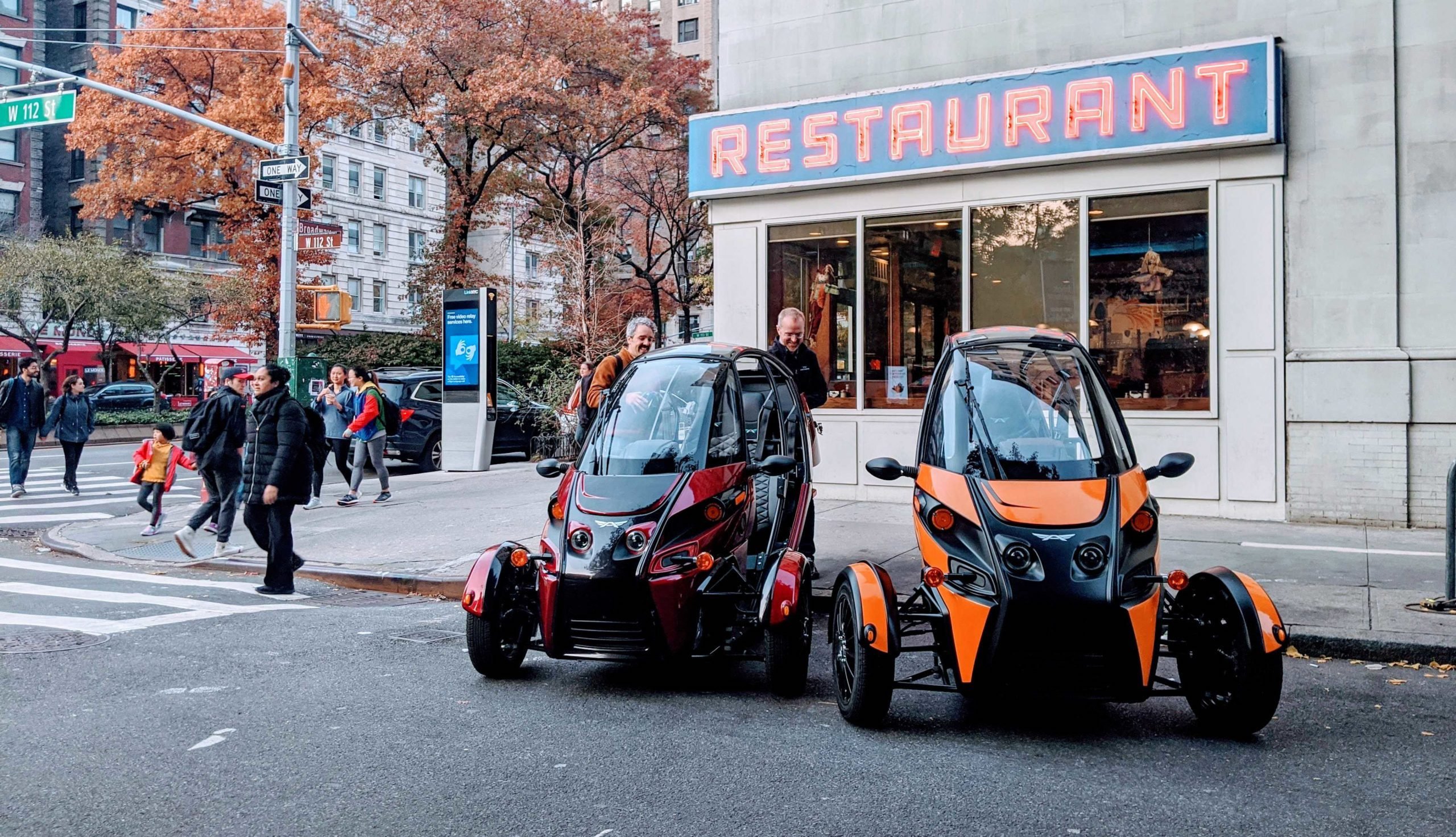 Arcimoto fun utility vehicles parked in front of a downtown restaurant 