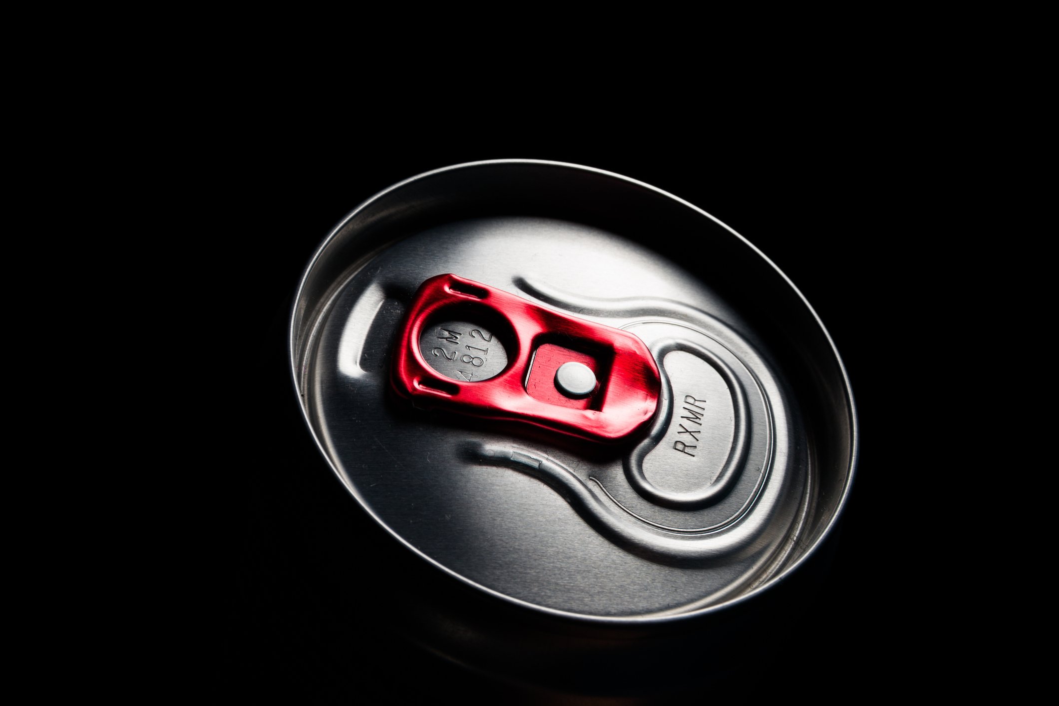 The illuminated top of an energy drink can against a dark background, with a red pull tab.