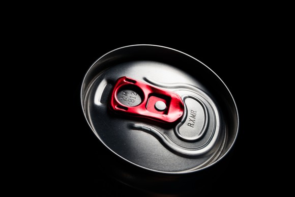 The illuminated top of an energy drink can against a dark background, with a red pull tab.