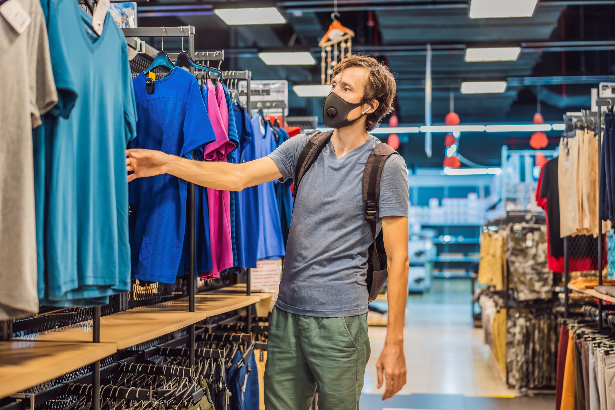 A man wearing a COVID-19 mask shopping shirts in an apparel store.