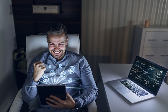 An investor pumps his fist in victory as he looks at stock market gains on his tablet.