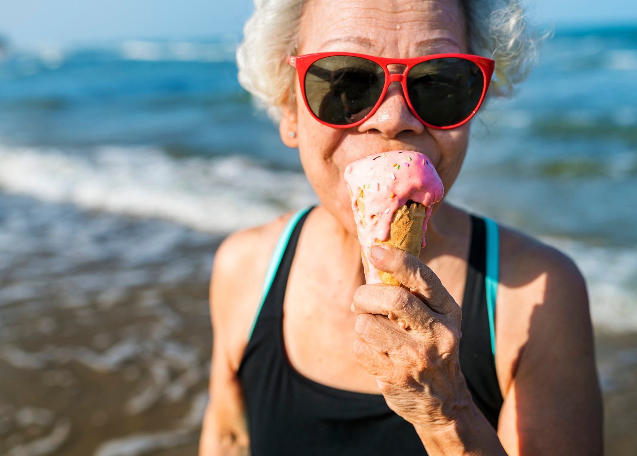 Senior woman in red sunglasses eating a strawberry ice cream cone.