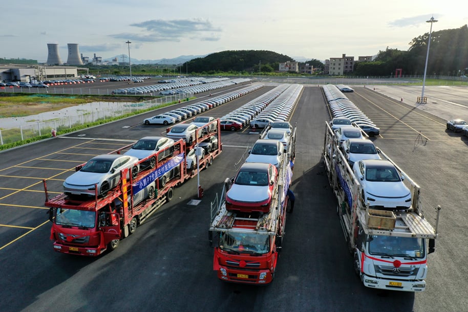 Car transporters loaded with Xpeng P7 sedans outside a factory.
