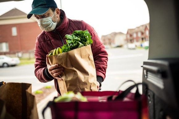 Home delivery of groceries by a delivery man wearing a face mask.