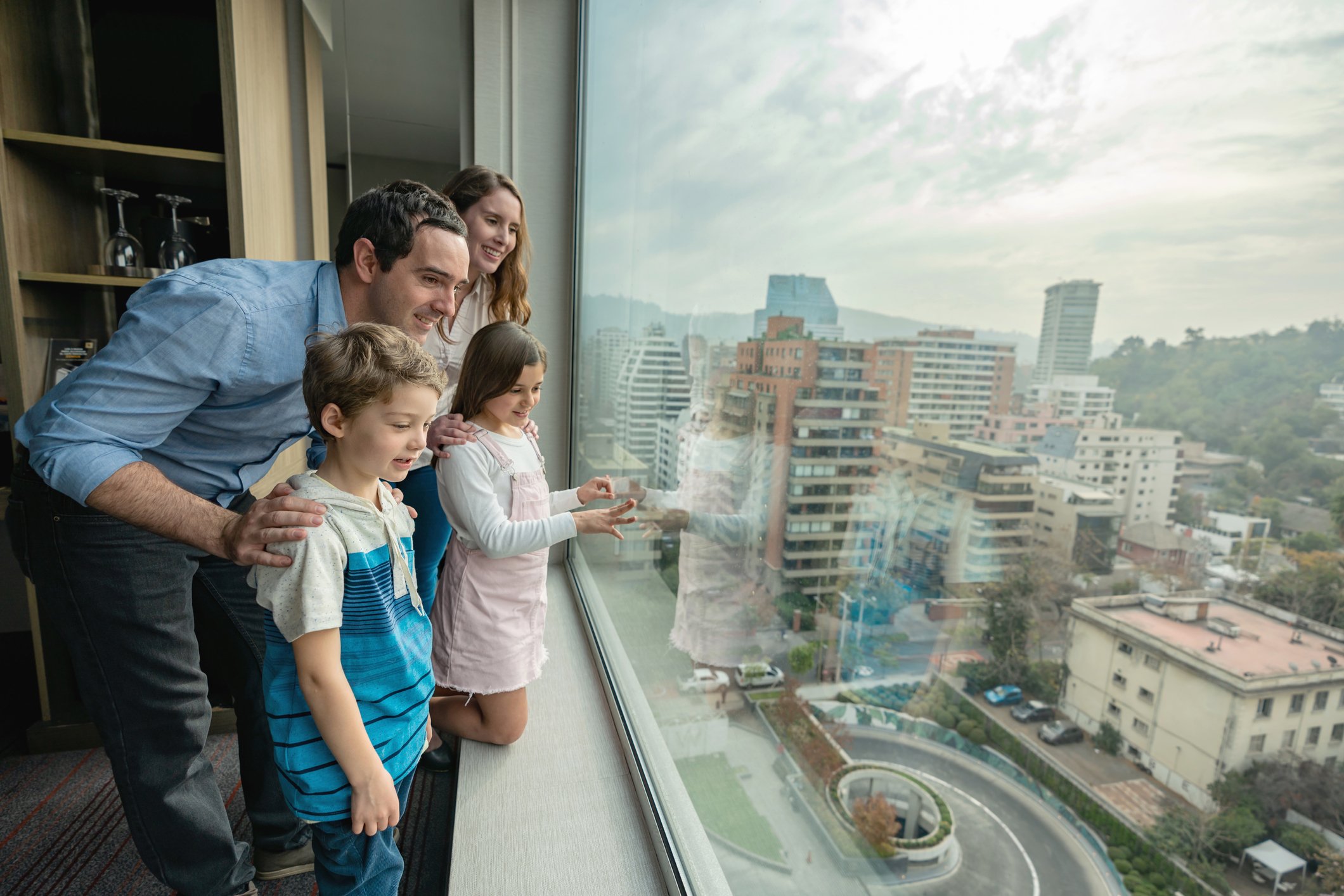 Excited family of four at their hotel bedroom looking at a beautiful window view all smiling