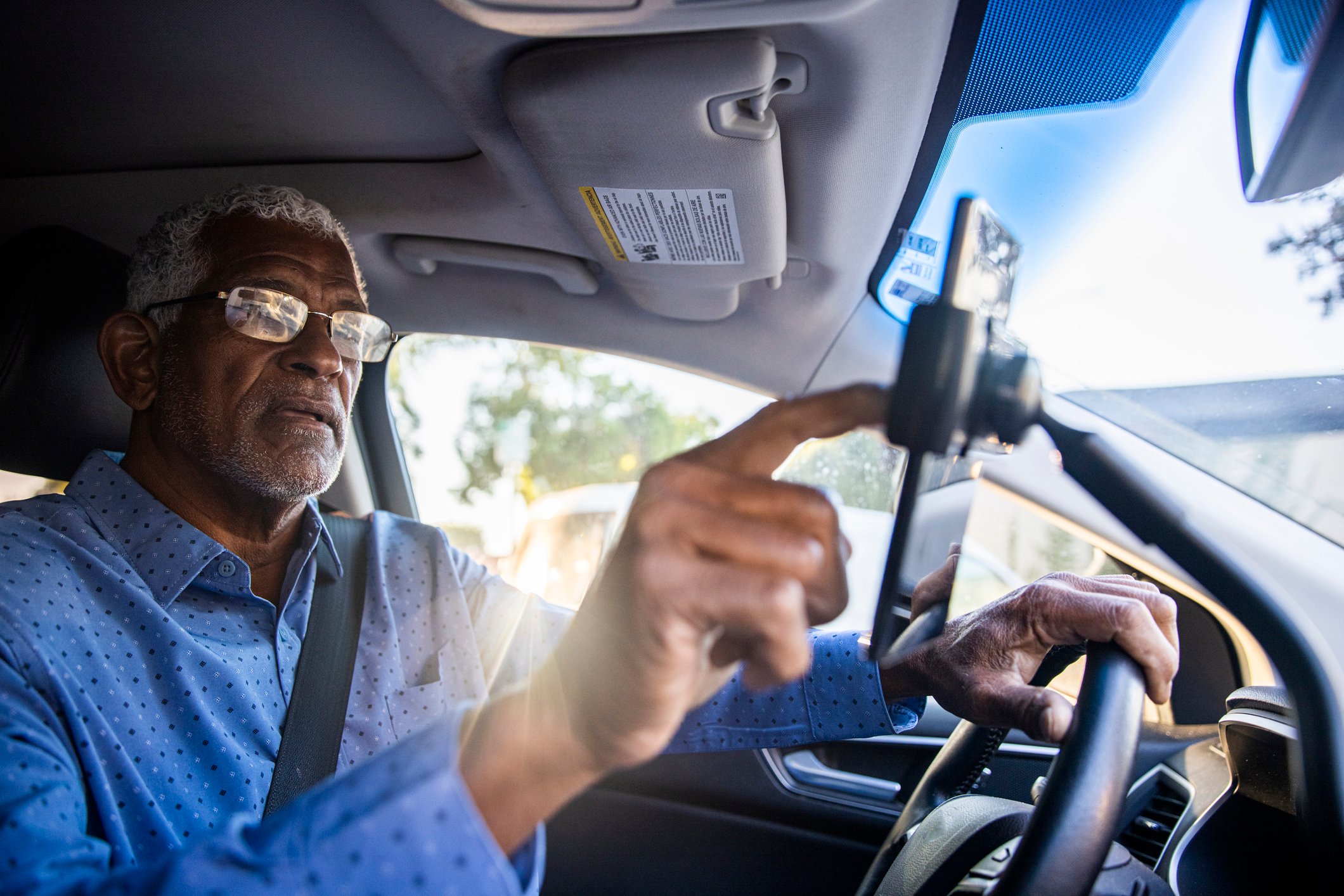 Senior gig worker using ride sharing app while in the driver's seat.