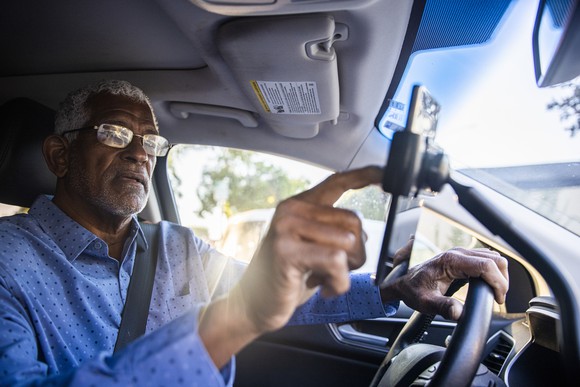 Senior gig worker using ride sharing app while in the driver's seat.