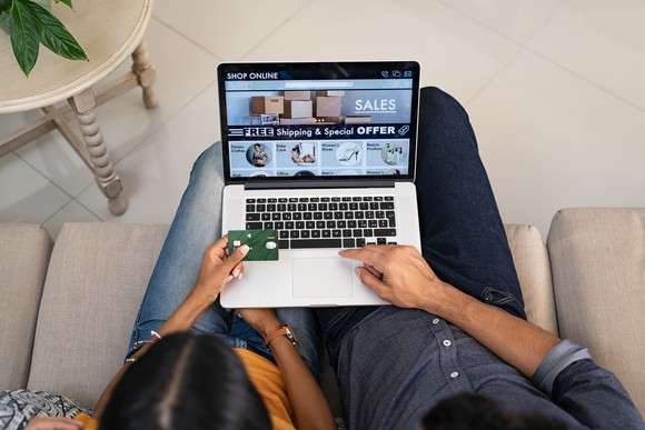 Two people sitting on the couch and shopping on a laptop.