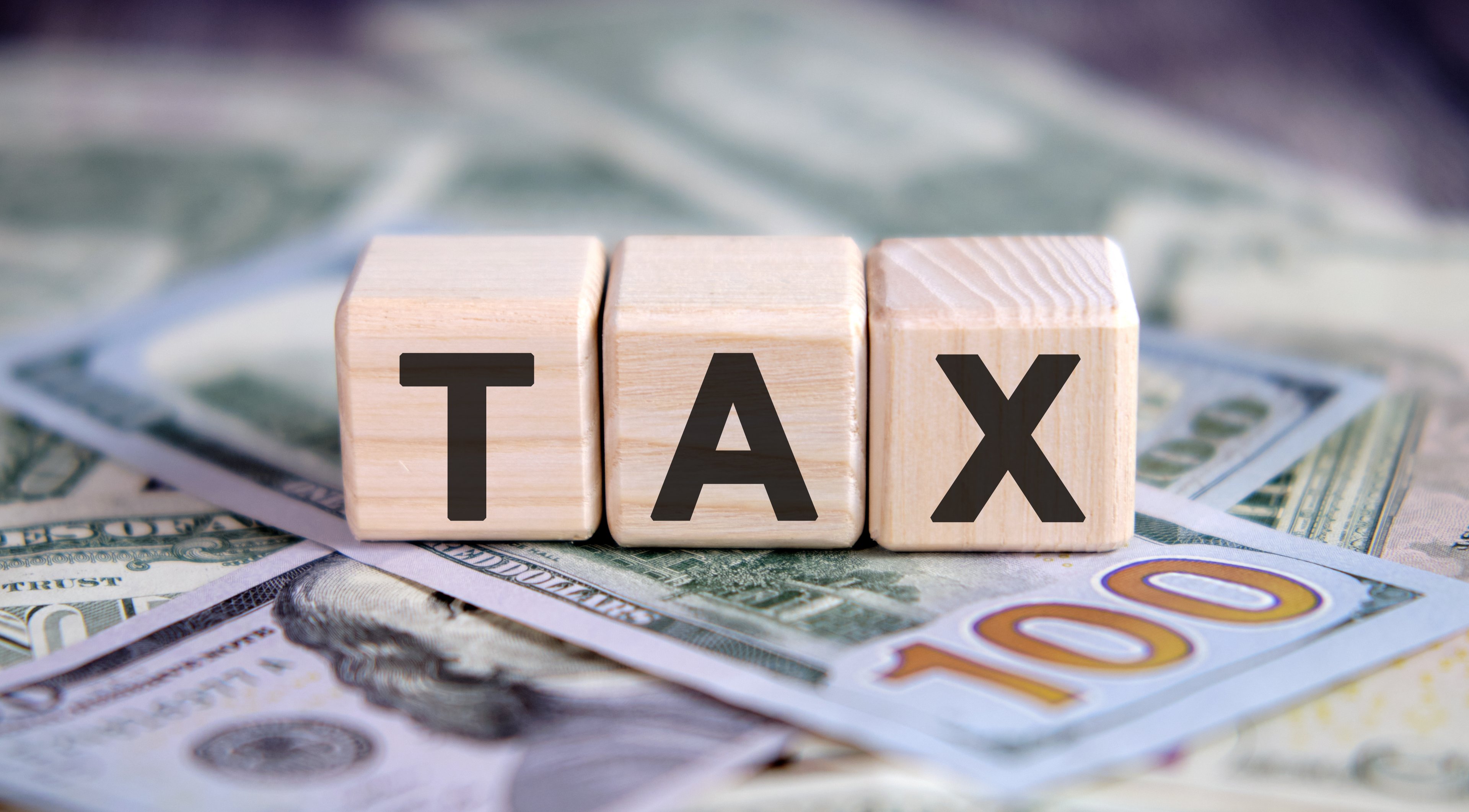 Tax - text on wooden cubes, on cash background.