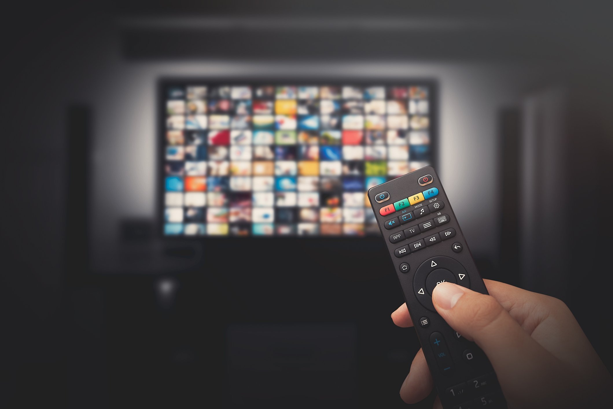 Man holding a smart TV remote in front of a television screen with many viewing choices.