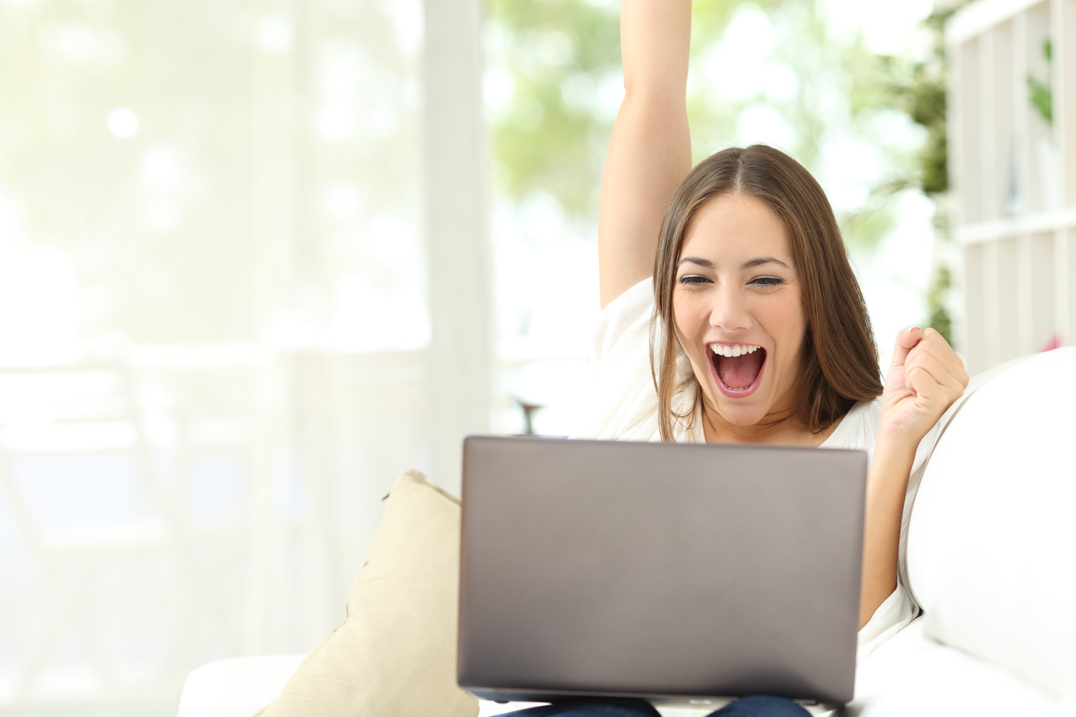 A lady celebrates good news on her laptop at home.